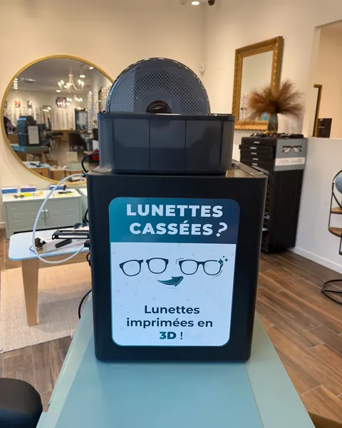 La machine d'impression 3D en boutique, avec l'affiche « Lunettes cassées ? Lunettes imprimées en 3D ! »